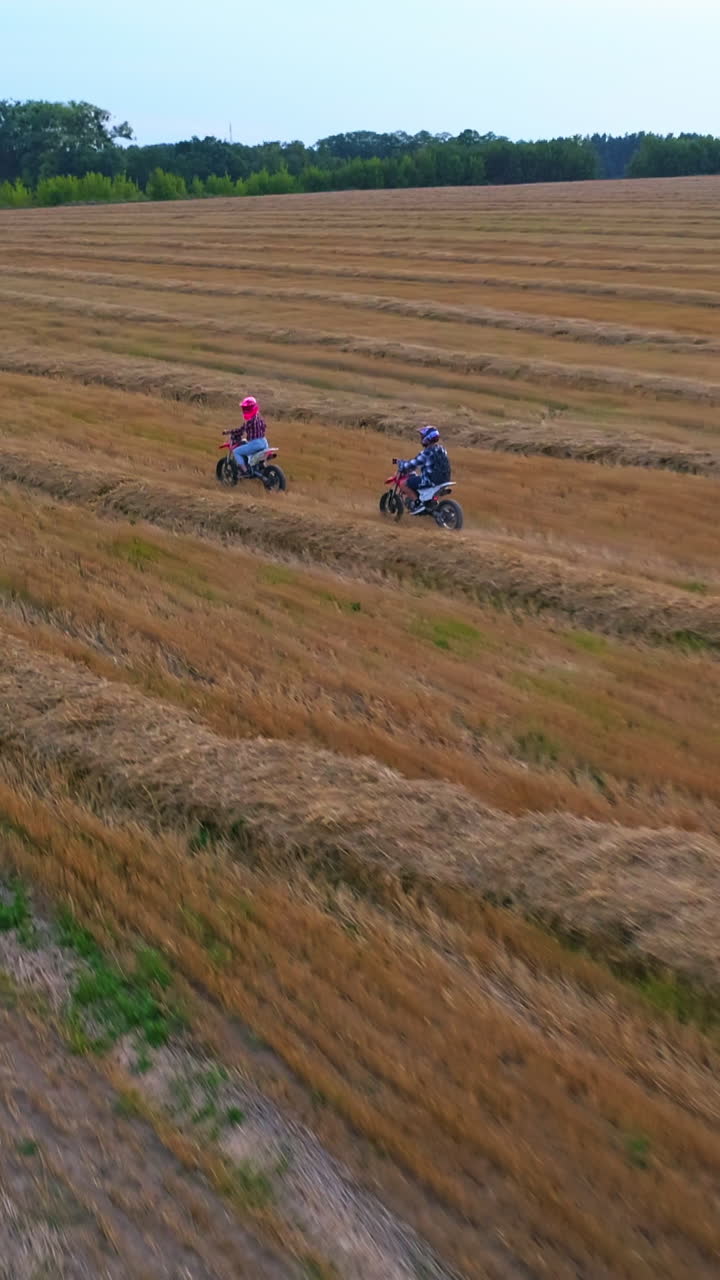 Two people riding motorbikes in the countryside. Girl in pink helmet riding first followed by her boyfriend. Top view. Vertical video