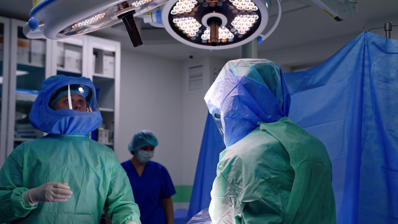 Læger i beskyttelseshjelme står under de runde lamper på operationsstuen. Forberedelse til traumeoperationen.