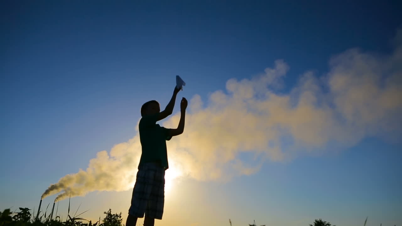 Boy With Paper Planes. Paper blue airplane in children hands at sunset near smoky pipes
