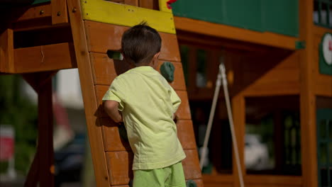 slow motion of a young latin boy on a climbing wall at a wooden playground on a sunny afternoon