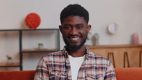 portrait of happy african american teenager student guy smiling looking at camera at home on sofa
