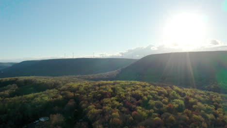 Smooth-cinematic-flight-over-green-forest-at-sunset-with-wind-turbines-on-far-away-mountains