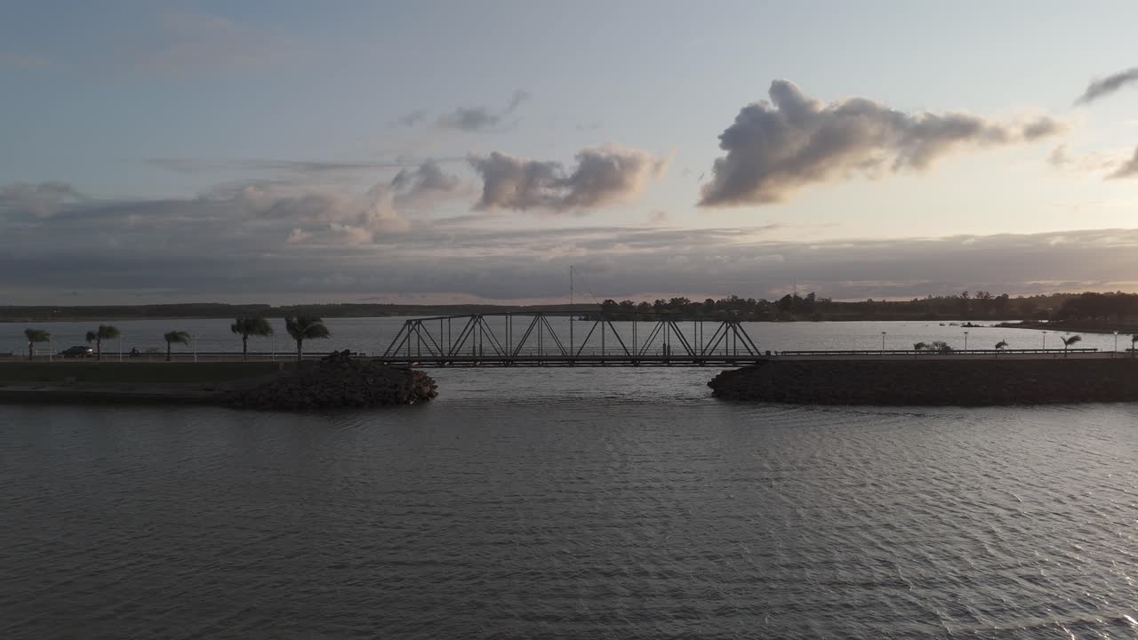 A serene landscape at dusk with a bridge silhouette against a tranquil water body under a cloud-streaked sky, capturing the peaceful beauty of the evening in Federacion, Entre Ríos, Argentina
