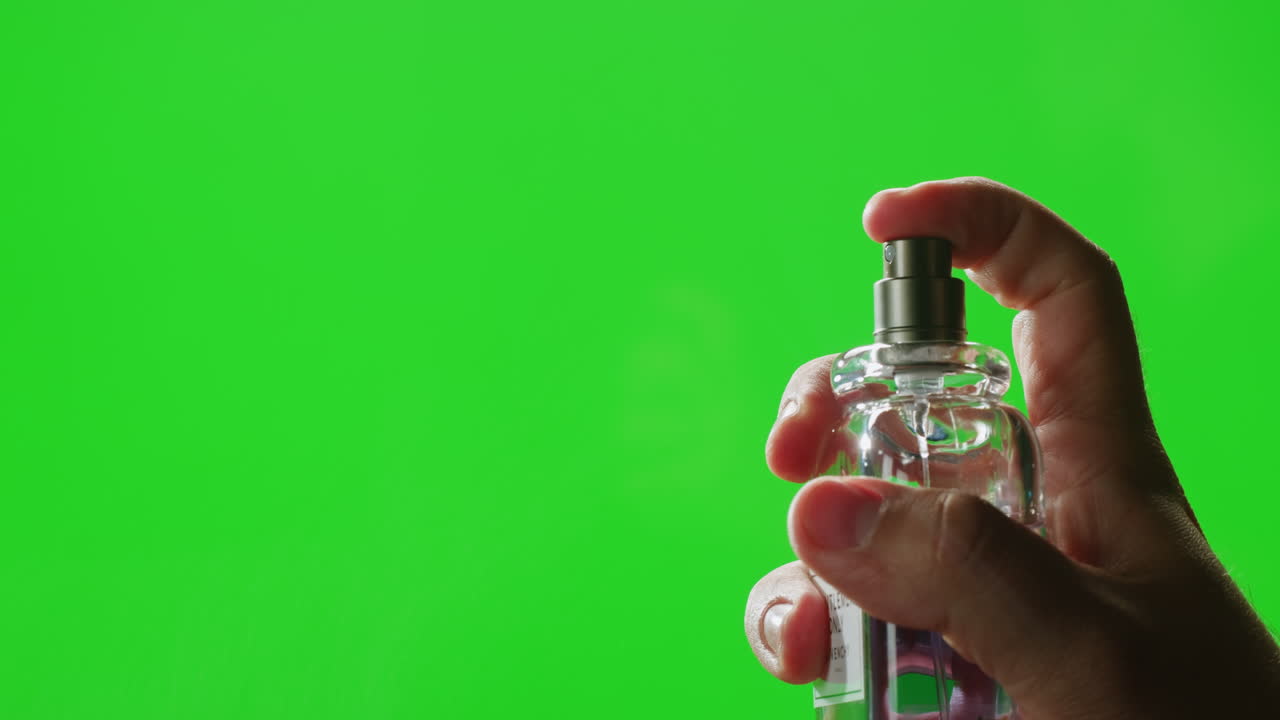 Hand spraying perfume on green screen