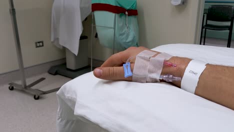 movimientos lentos de la mano de la mano derecha masculina caucásica irreconocible en un escenario médico con iv en la muñeca