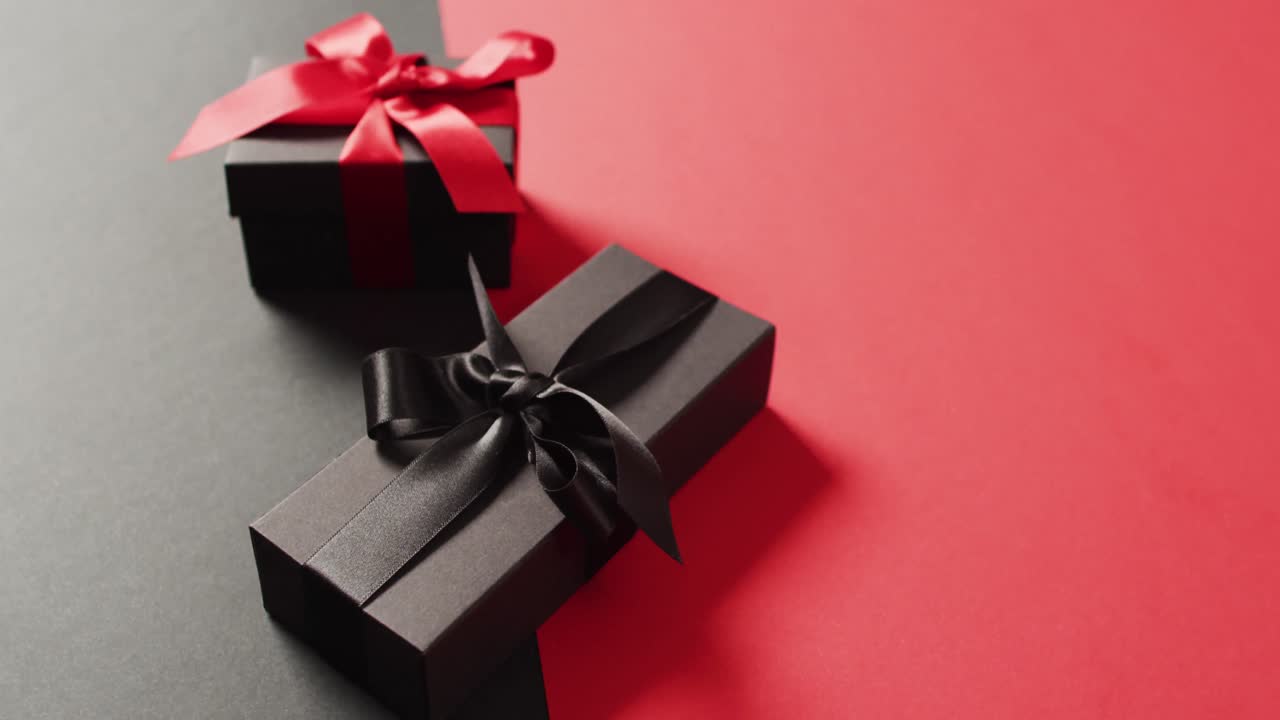 dos cajas de regalos negras con cintas rojas y negras en fondo negro y rojo con espacio para copiar