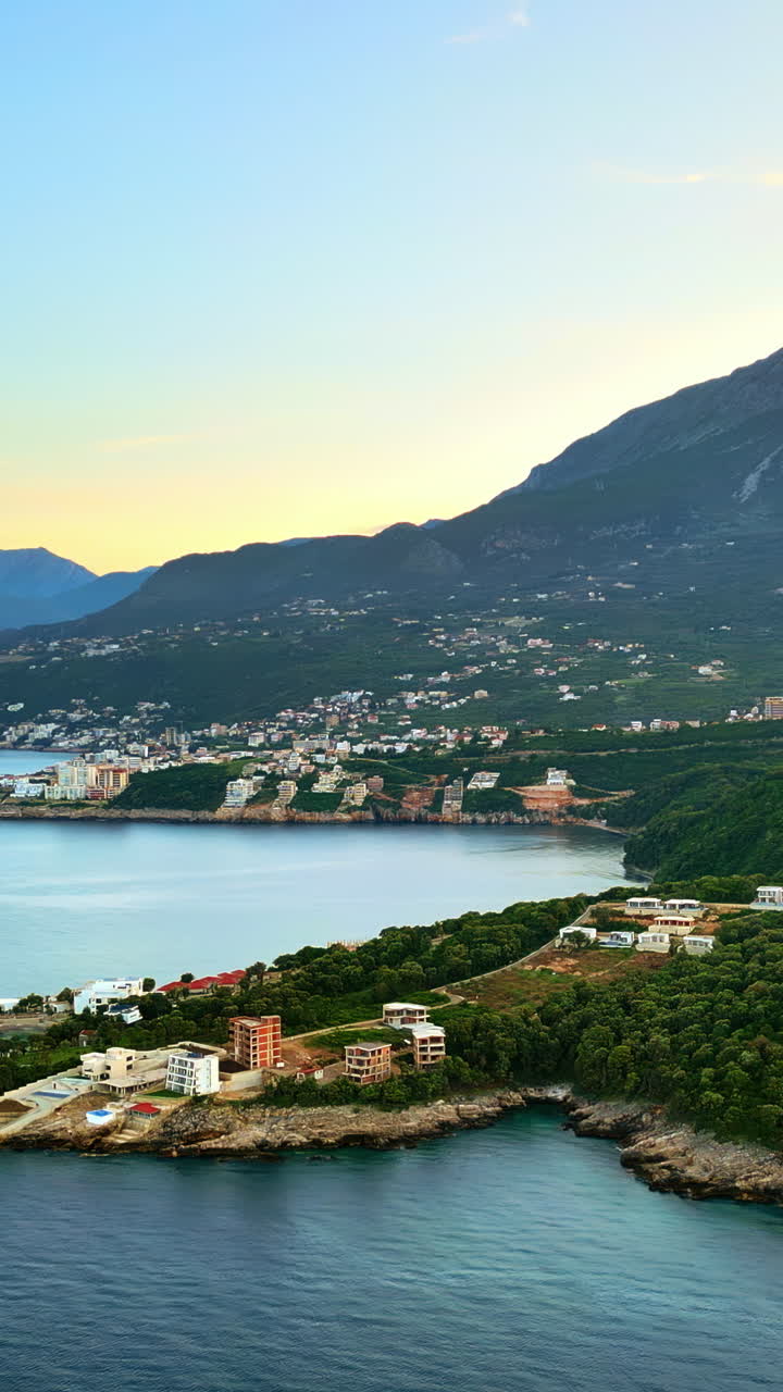 Aerial, drone view of buildings on the shore of the Adriatic sea, with mountains on the background in Montenegro. Vertical