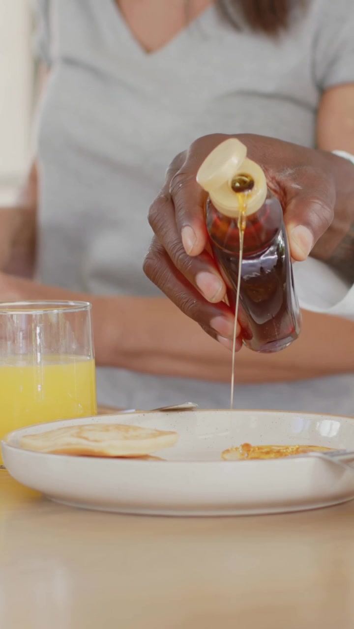 Video verticale: Una mano con manica bianca che versa sciroppo sui pancake a casa per la colazione con succo d'arancia.