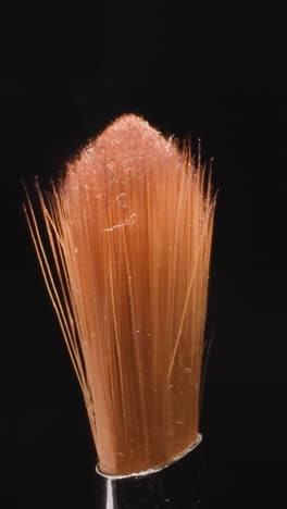used old brush with glitter on orange bristles used for eye makeup. professional cosmetic product for applying eyeshadows on black background macro
