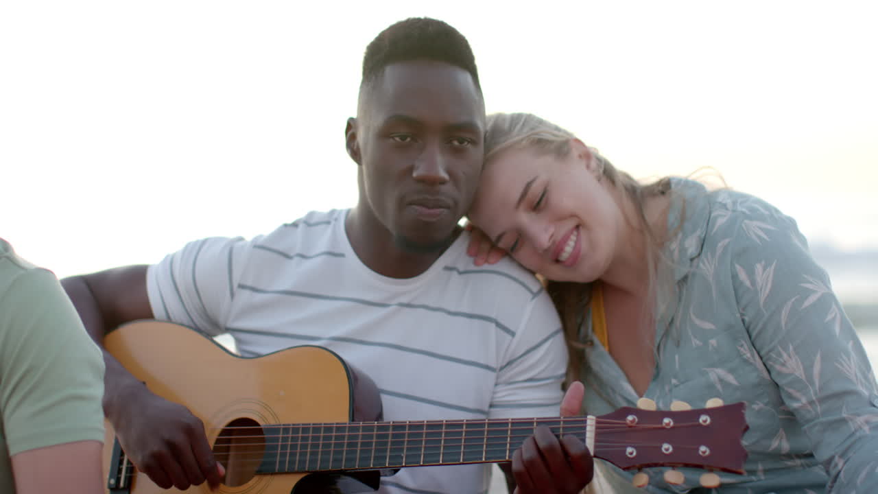 Giovane uomo afroamericano suona la chitarra all'aperto a una festa in spiaggia