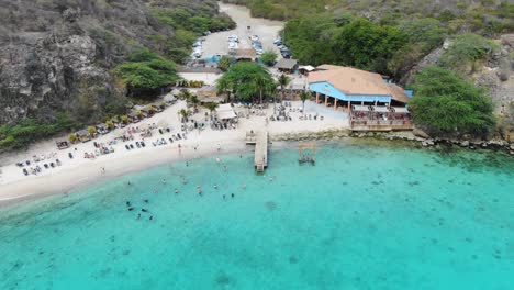 kokomo beach in curacao with people swimming and lounging on the sand, vibrant turquoise water, aerial view