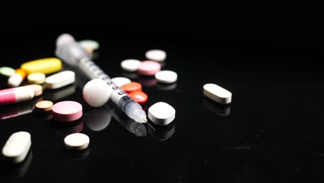 syringe and assorted pills on black surface