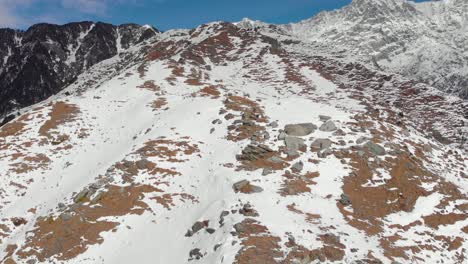 aerial truck-up shot of two people hiking to the top of triund peak with snow patches covered around them during the winters shot with a drone in 4k