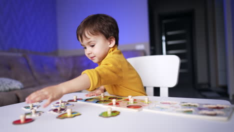 baby boy in yellow sweater reaches for a puzzle piece. toddler kid playing with puzzles at home.
