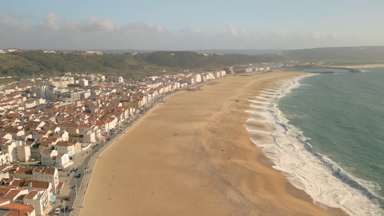 Ripresa aerea della spiaggia di Nazaré dalla sabbia dorata con le onde che si infrangono sulla riva