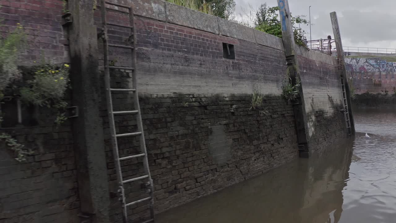 Drone view over dark water of old harbor with shabby brick walls and metal ladders in modern city
