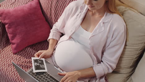 mujer embarazada con una imagen de ultrasonido fetal y usando una computadora portátil