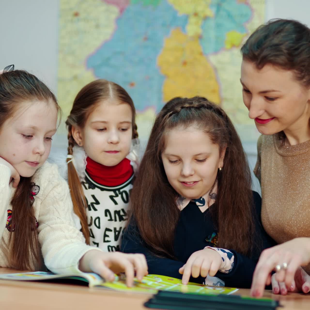 Learning process at primary school. Young female teacher sitting together with little schoolgirls and studying at school. Education concept.
