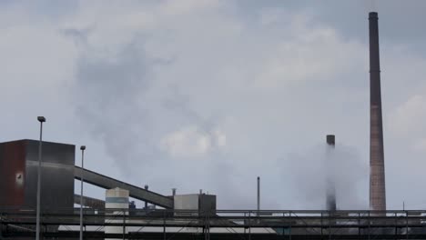 industrial plant emitting smoke against a cloudy sky, suggesting pollution, environmental impact