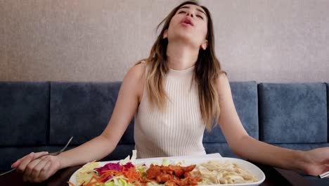 cámara lenta: hermosa joven come comida de pollo con un gran disfrute en un restaurante o cafetería mientras está sentada