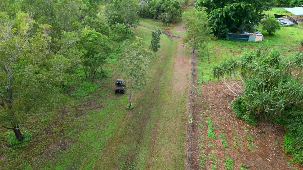 Ripresa aerea con drone di un buggy che guida su una proprietà residenziale in una tenuta rurale coperta da una rada foresta dell'outback