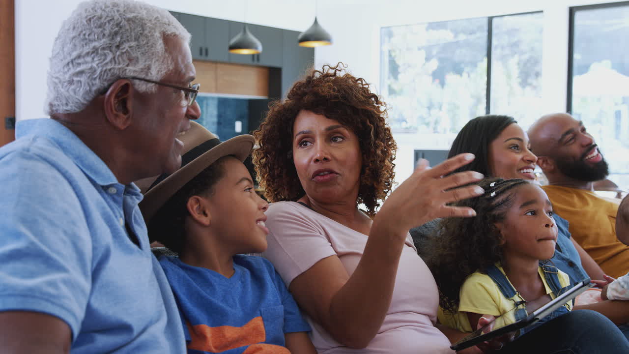 Multi-Generation African American Family Relaxing At Home Sitting On Sofa Watching TV Together