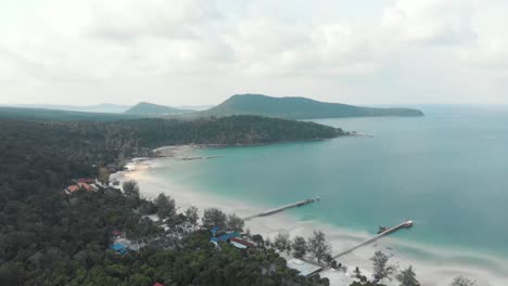 wooden beach piers entering the blue shallow sea in the paradisiac saracen bay in koh rong sanloem, cambodia - aerial wide fly-over shot