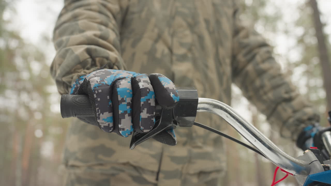 Closeup gloved hand on atv throttle in pine forest practices precise control and balance, camo jacket and helmet in soft winter light, handlebar and LED light visible, repeated grip adjustments show