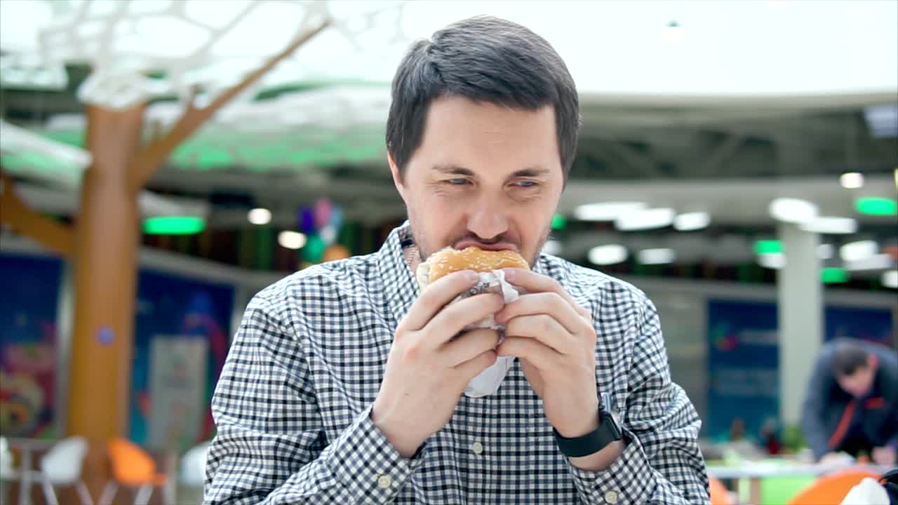hombre comiendo una hamburguesa en una sala de comidas del centro comercial