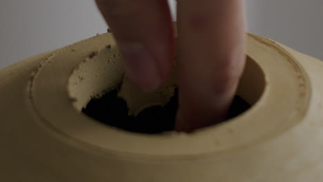 close up shot of removing clay from the hole of a pottered vase after the lid was removed with a special tool