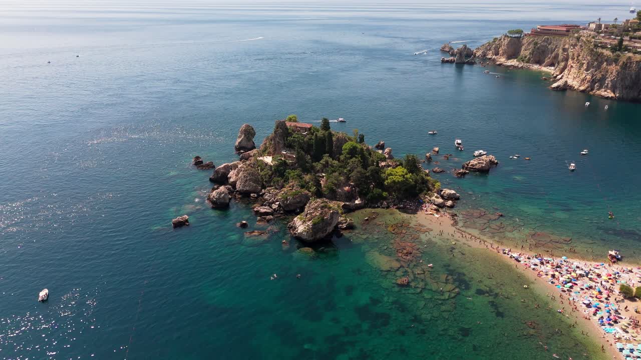 Drone slowly pans right to left around Isola Bella, showcasing the island, coastline, and sandy beach in a serene aerial view