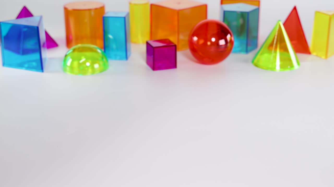 A hand interacts with vibrant 3D geometric shapes on a white surface, demonstrating movement and arrangement