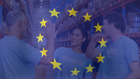 animation of flag of european union over diverse male and female volunteers high fiving in warehouse