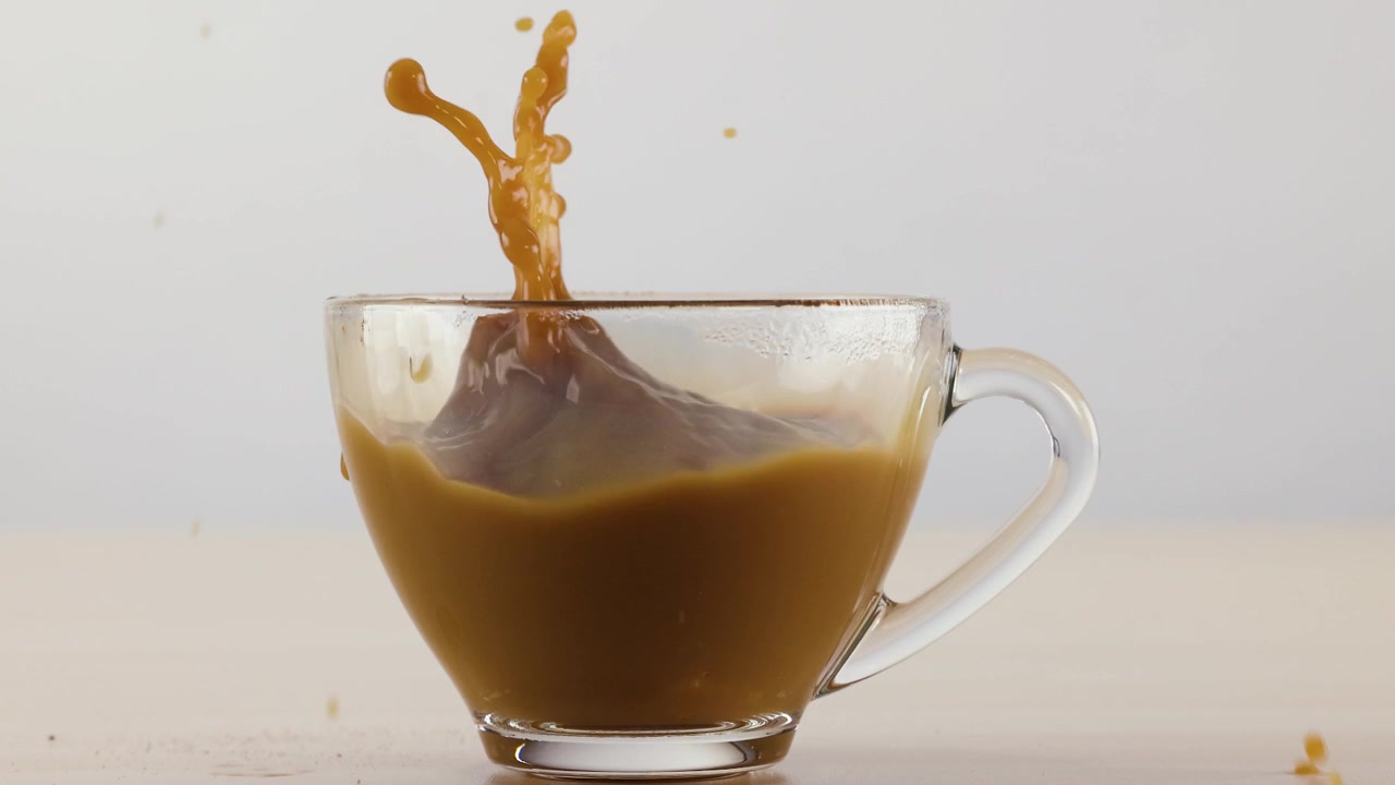 Ripresa al rallentatore di caffè latte che schizza all'interno di una tazza di vetro trasparente su sfondo bianco.