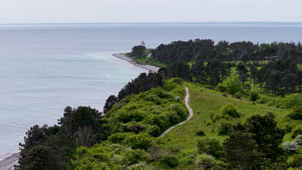 Aerial drone footage of Sletterhage Lighthouse on the Djursland peninsula in Denmark, showing the coastline, forest, and winding road along the shore