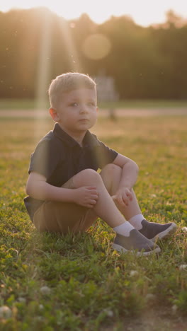 little boy sits in flying insects swarm on lush grass at sunset slow motion. using repellent to protect children from bites. safety in summer