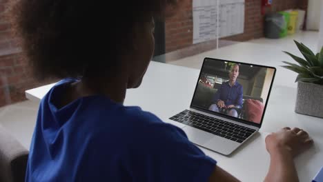 Back-view-of-african-american-woman-having-a-video-call-on-laptop-with-male-colleague-at-office