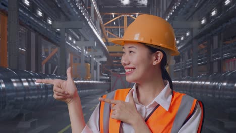 Close Up Of Asian Female Engineer With Safety Helmet Smiling And Pointing To Side While Standing With Metal Pipes