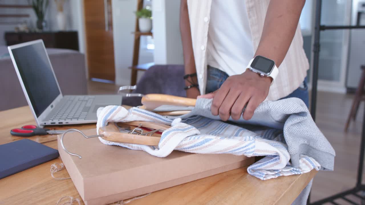 Vertical video: Man lifting striped shirt from box, inspecting and arranging hangers for e-commerce