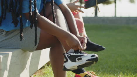 vista lateral de mujeres sentadas en un banco y atando zapatillas de deporte