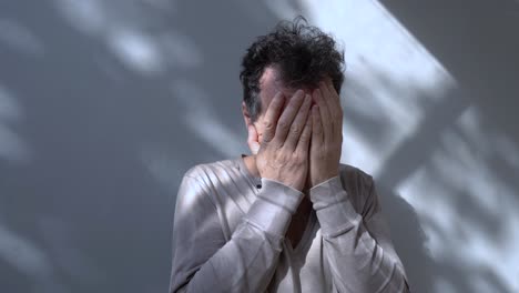 a middle-aged man with disheveled hair holds his face with both hands, expressing deep concern or stress