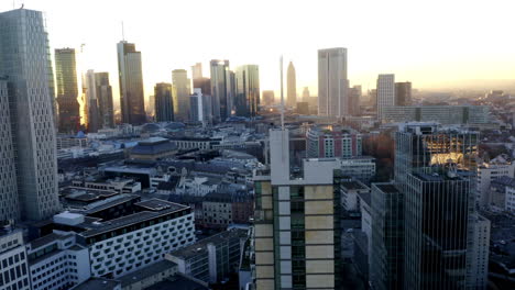 AERIAL:-Confident-Young-Man,-Guy-standing-on-rooftop-in-Skyline-of-Frankfurt-am-Main,-Germany-with-Beautiful-Sunlight-in-Winter-Haze