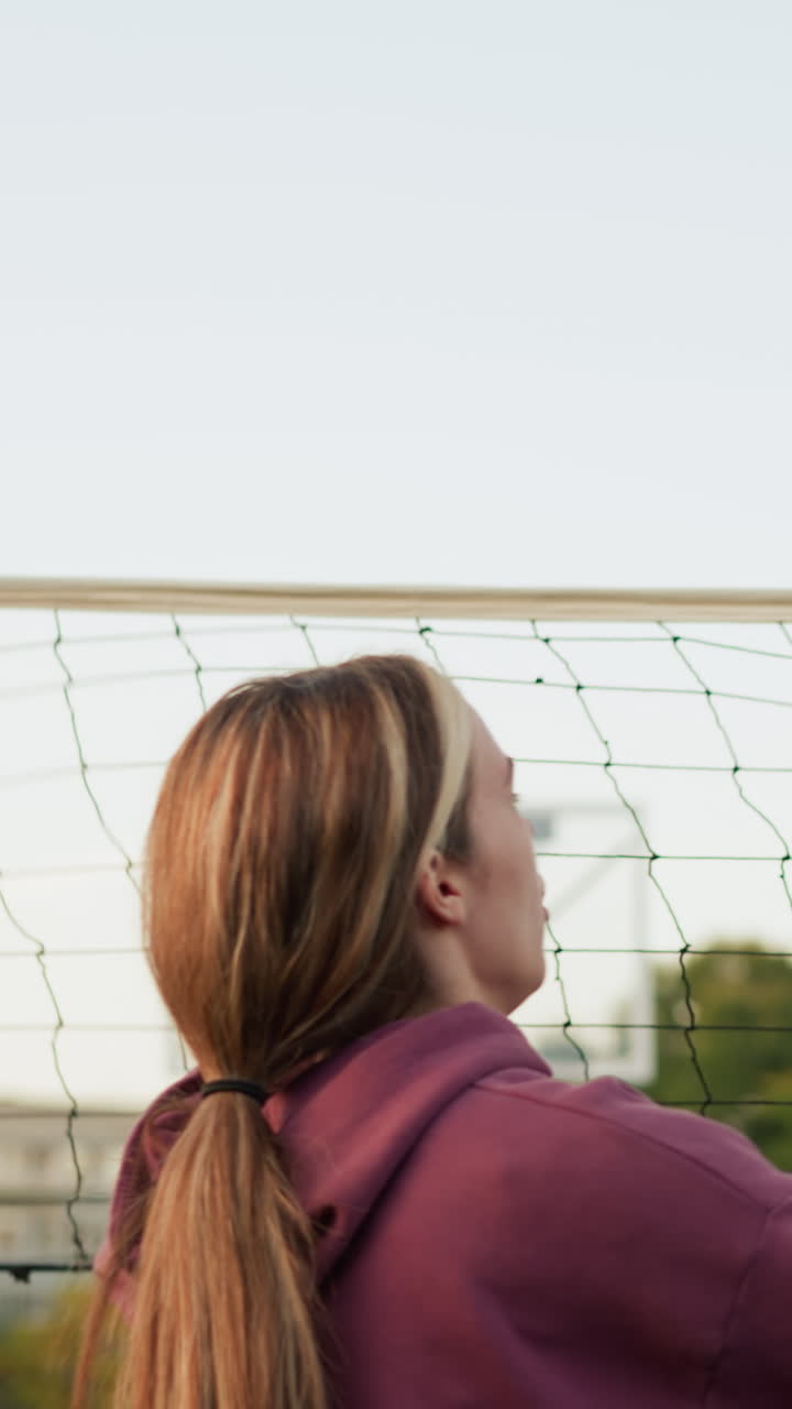 Back view of women playing volleyball, one player prepares to hit ball while teammates on the other side of net play against them, volleyball court and net in background