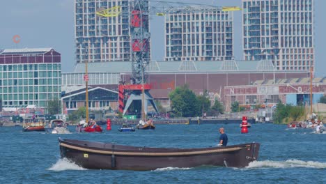 single motorboat moves across amsterdam river, daytime, modern buildings, wide shot, steady camera