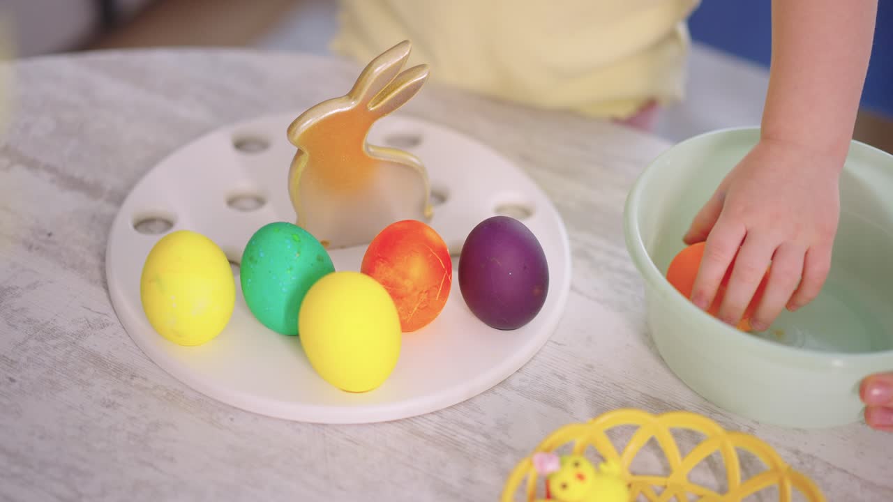 Child's Hand Arranging Colorful Easter Eggs on a Tray