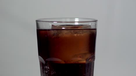 gran cubo de hielo girando en un vaso de bebida con cola en el fondo gris del estudio - primer plano estático