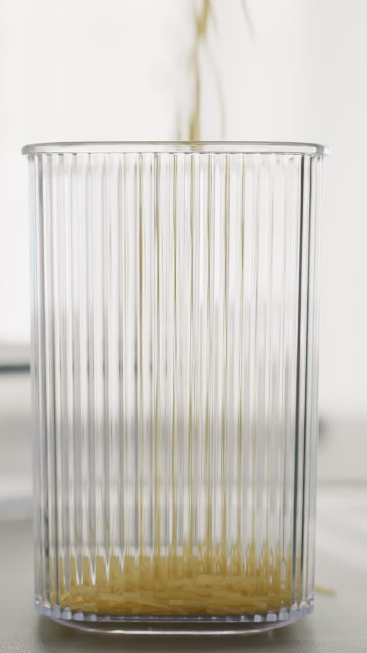 스파게티는 테이블 위의 높은 플라스틱 용기에 떨어집니다. 요리사는 요리하기 전에 원시 제품의 일부를 습니다. 사람은 부에서 집안 일을합니다.