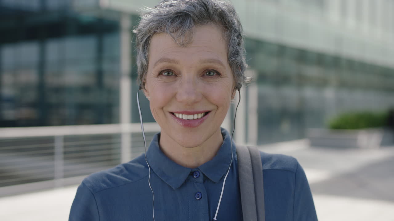 ritratto di una donna d'affari matura e professionale che sorride felice, indossa auricolari e si diverte ad ascoltare musica sullo sfondo della città urbana
