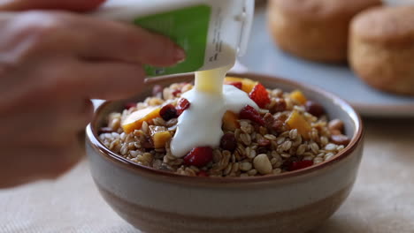 pouring yogurt into a bowl of granola with fruit and nuts