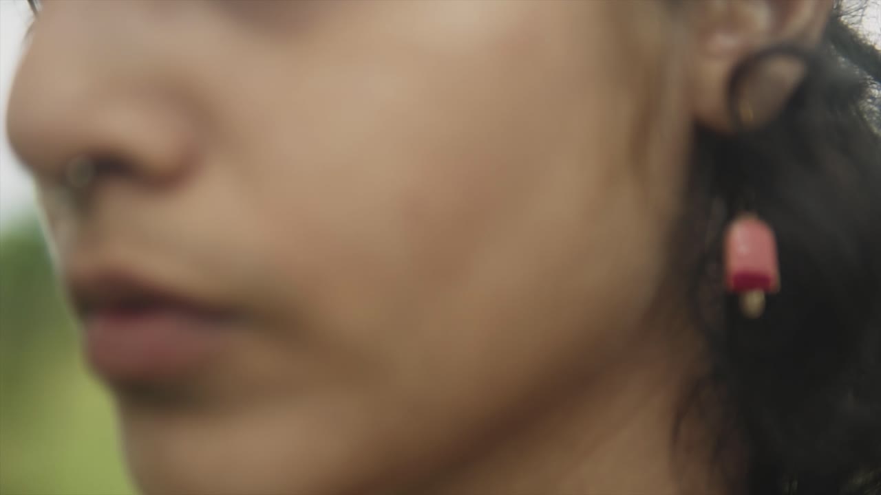 un acercamiento extremo acercándose a la cara y el pómulo de una joven y atractiva mujer asiática milenaria parada en un campo al aire libre, india